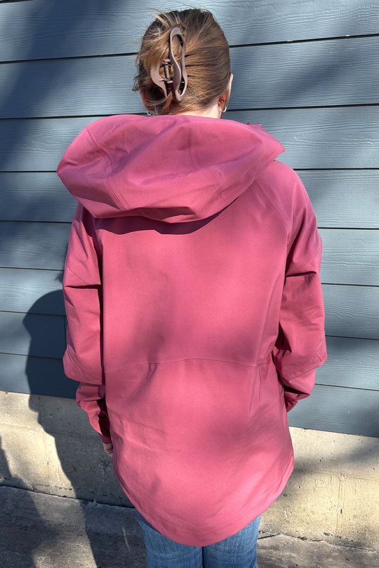 Person wearing a pink hooded jacket standing against a blue wall.