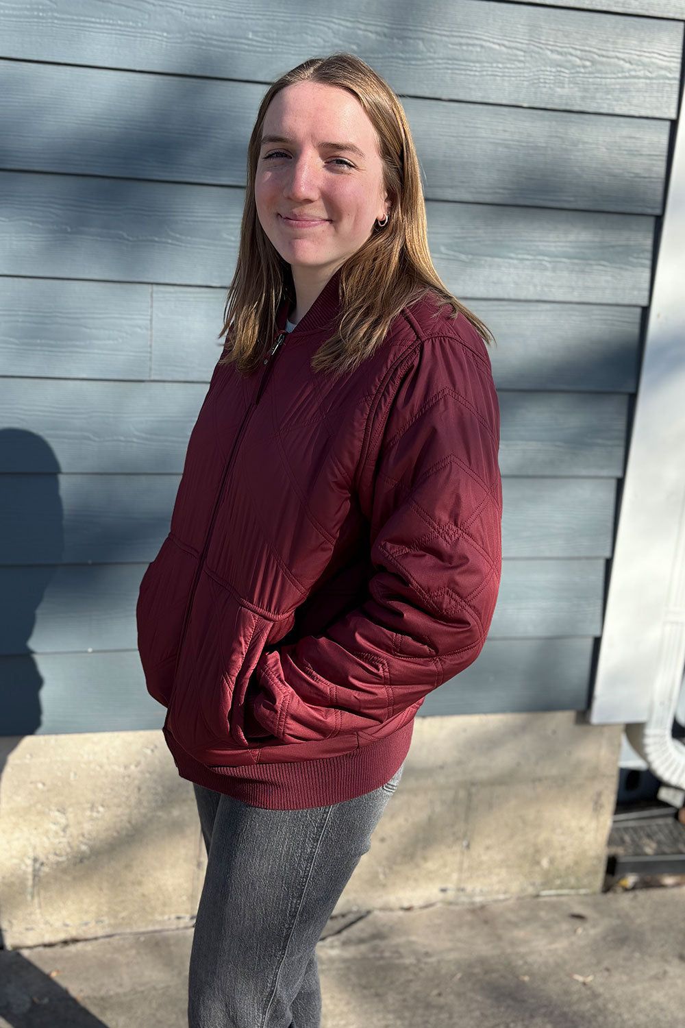 Person wearing a maroon jacket standing against a gray wall.