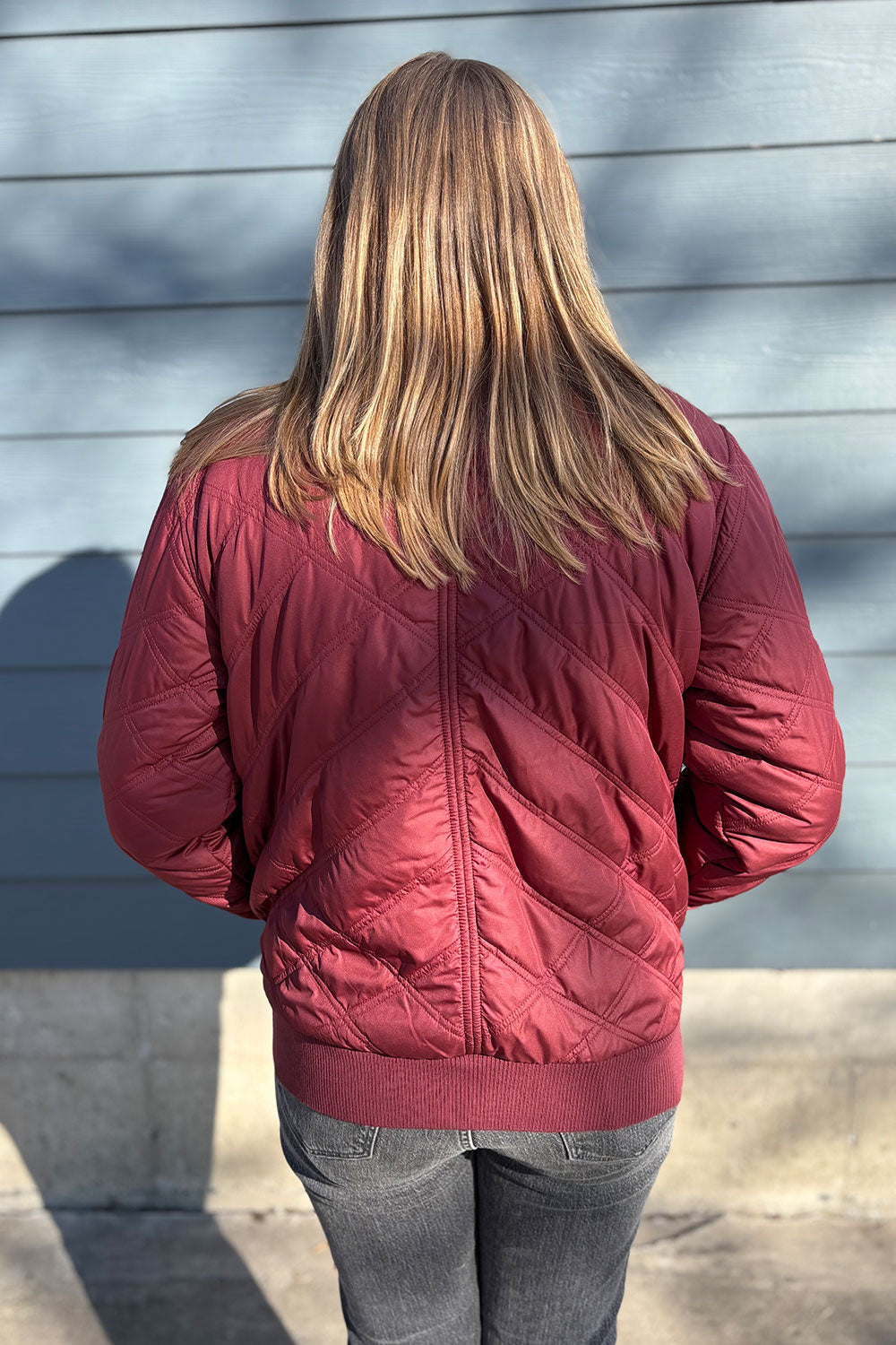 Person wearing a red quilted jacket standing against a gray wall.