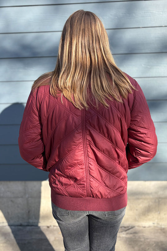 Person wearing a red quilted jacket standing against a gray wall.