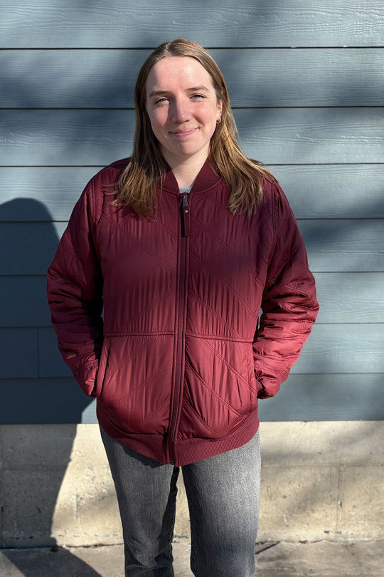 Person wearing a red jacket standing against a gray wall.