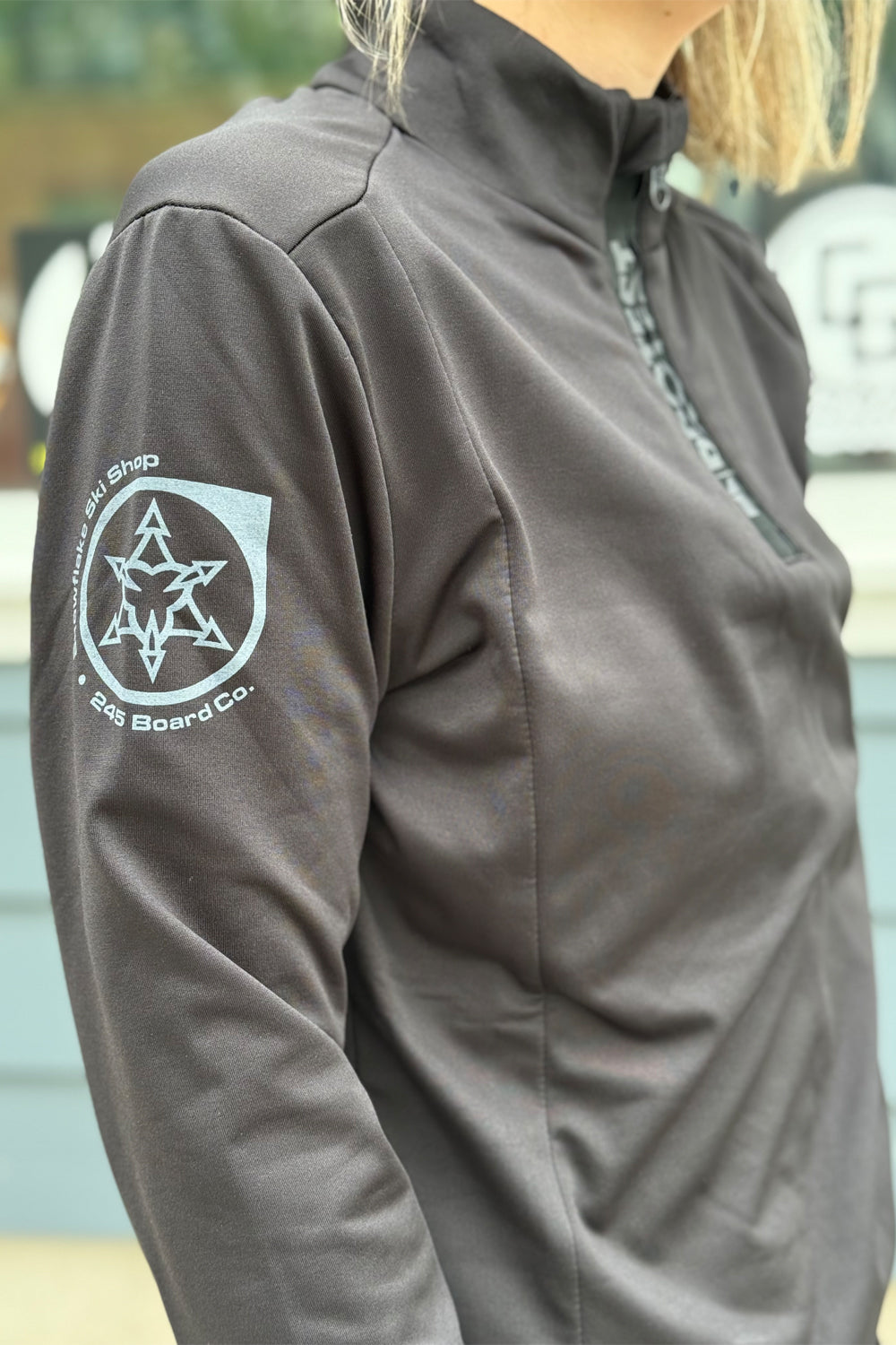 Close-up of a black 1/4 zip top with a logo on the sleeve, blurred background