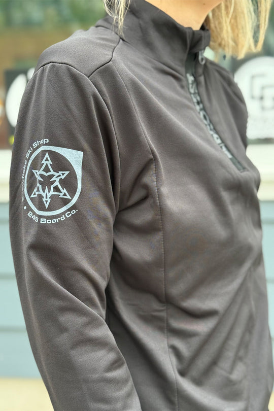 Close-up of a black 1/4 zip top with a logo on the sleeve, blurred background