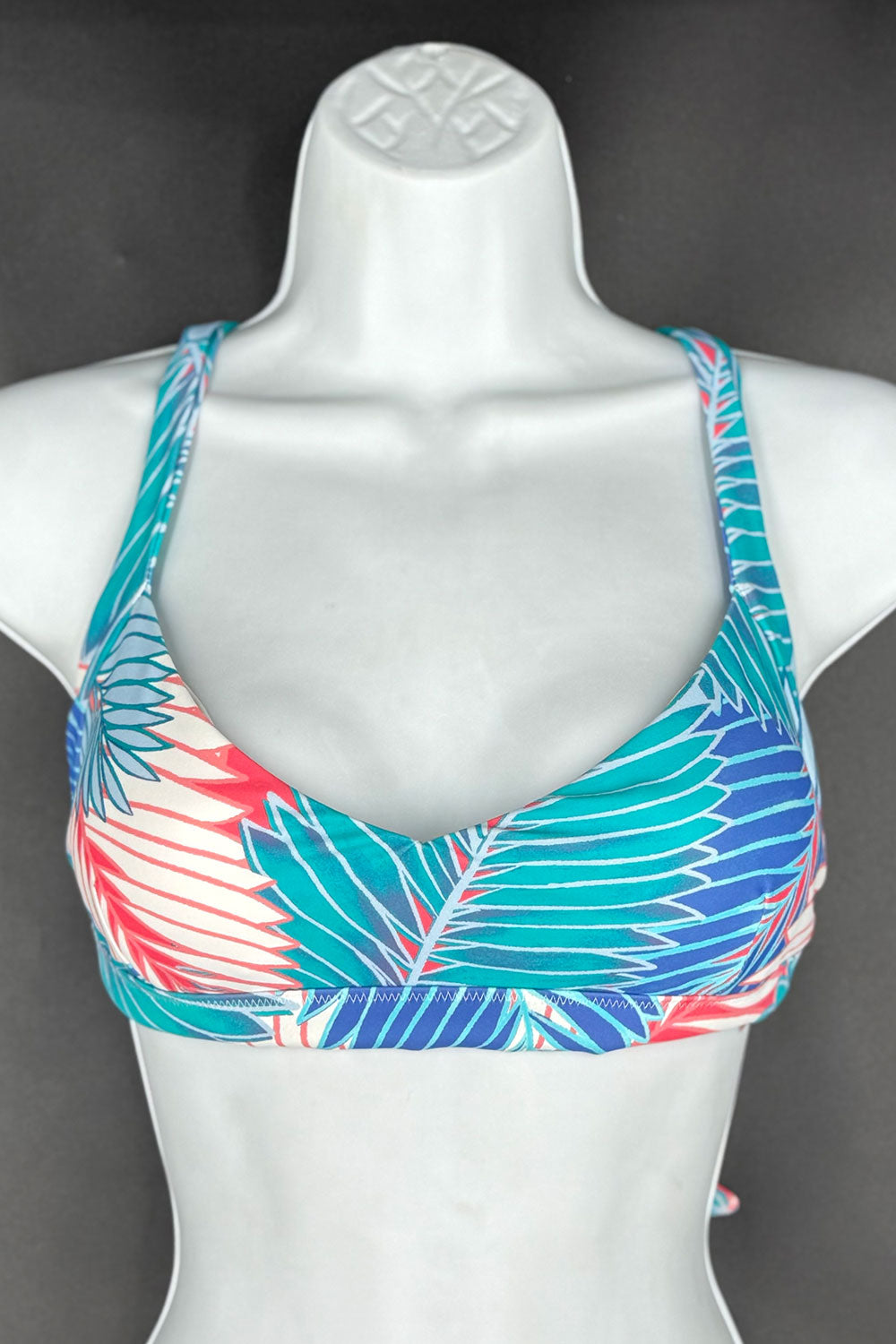 Colorful leaf-patterned bikini top on a mannequin against a dark background