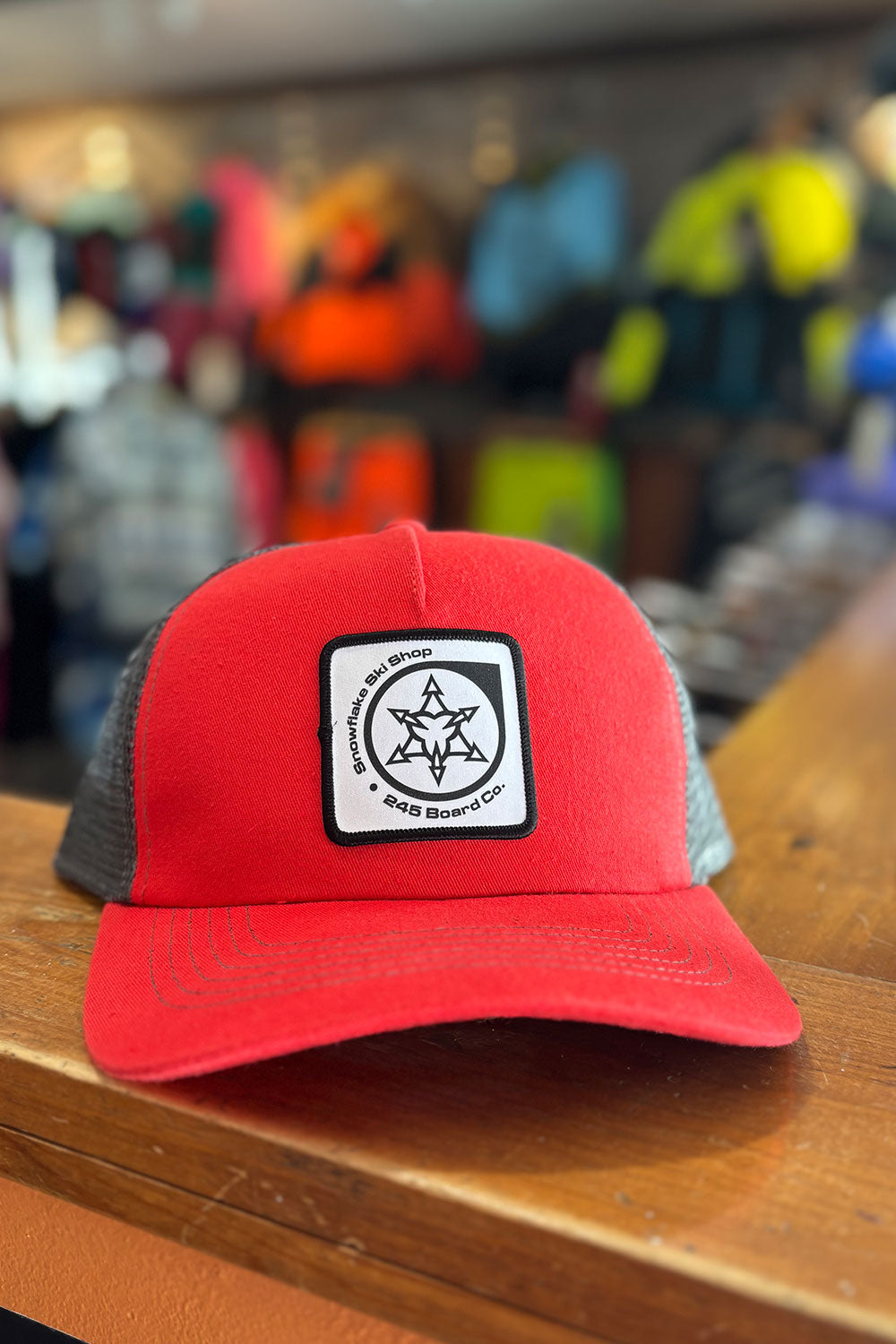 Red and gray cap with a logo on a wooden surface with a blurred background of colorful items.