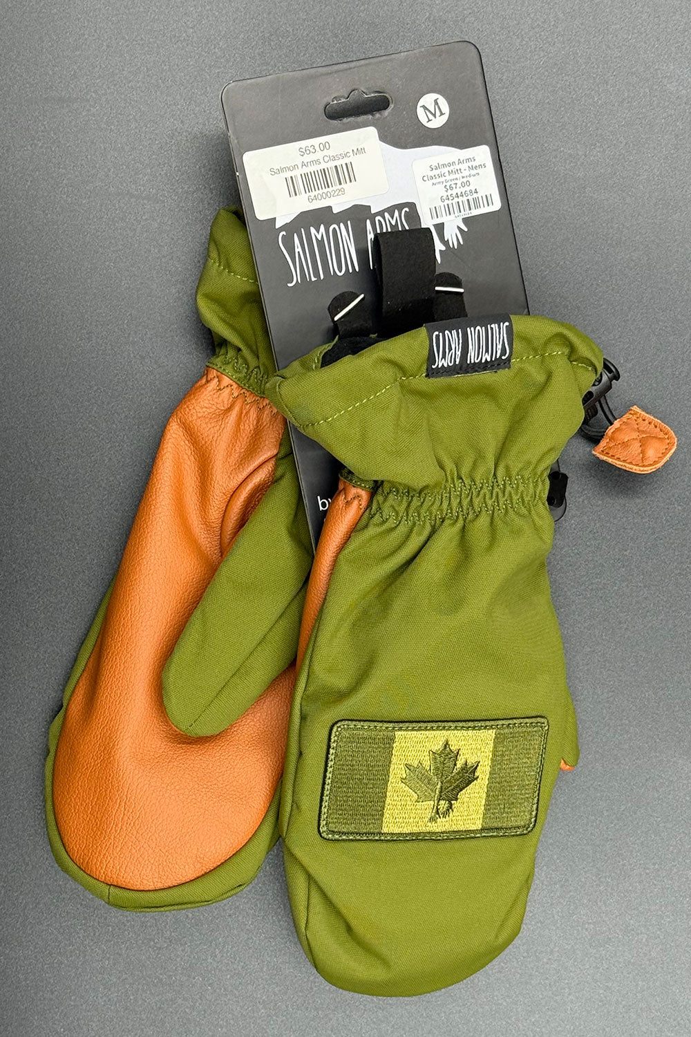 Green and orange mittens with a brand label on a gray background