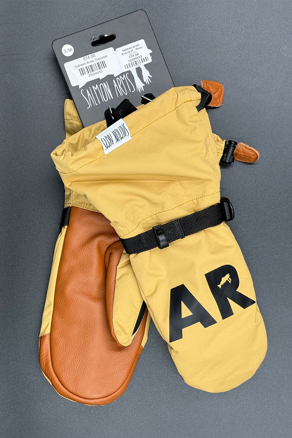 Pair of yellow and brown mittens with 'Salmon Arms' branding on a gray background