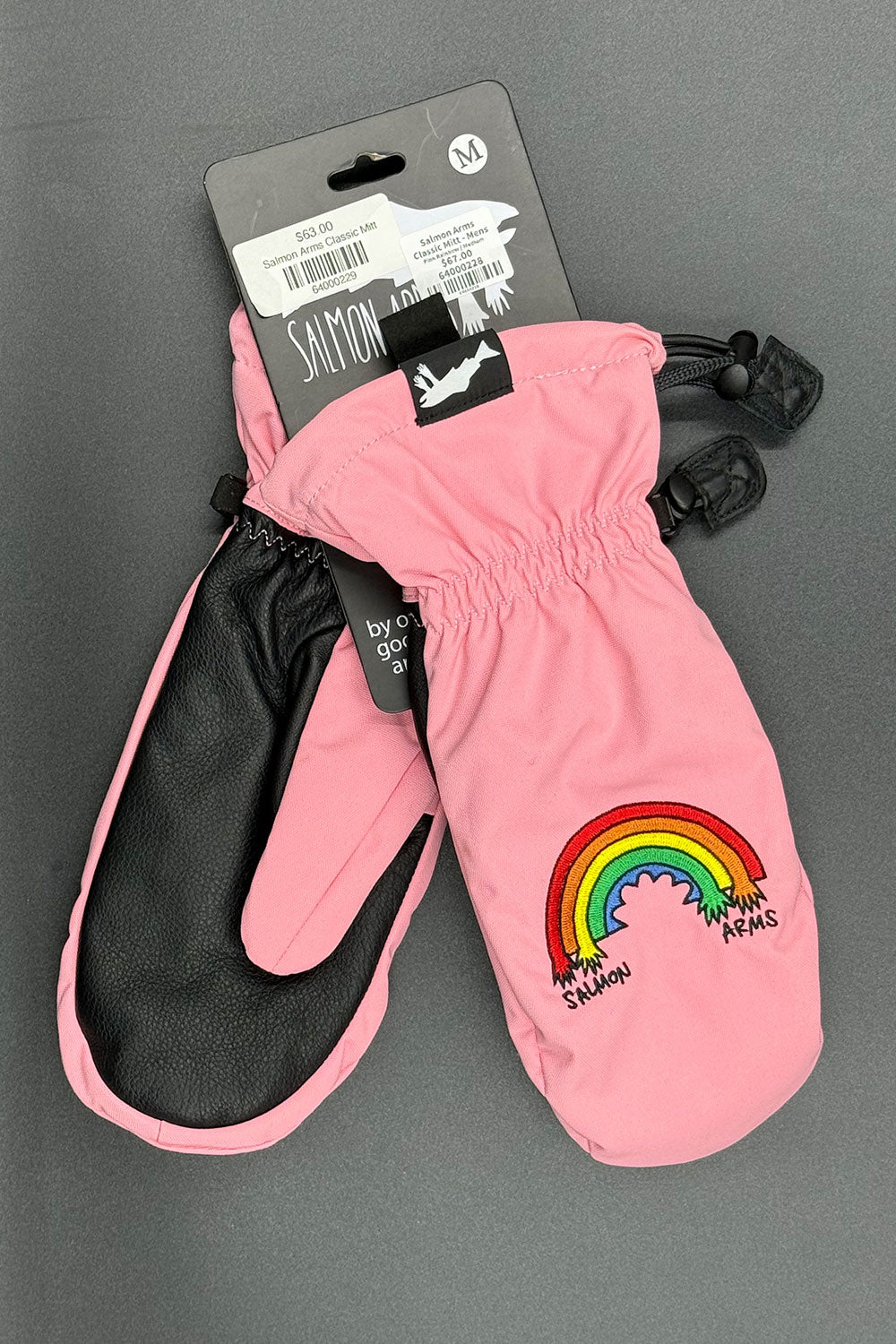 Pink mittens with black cuffs and rainbow design on a gray background