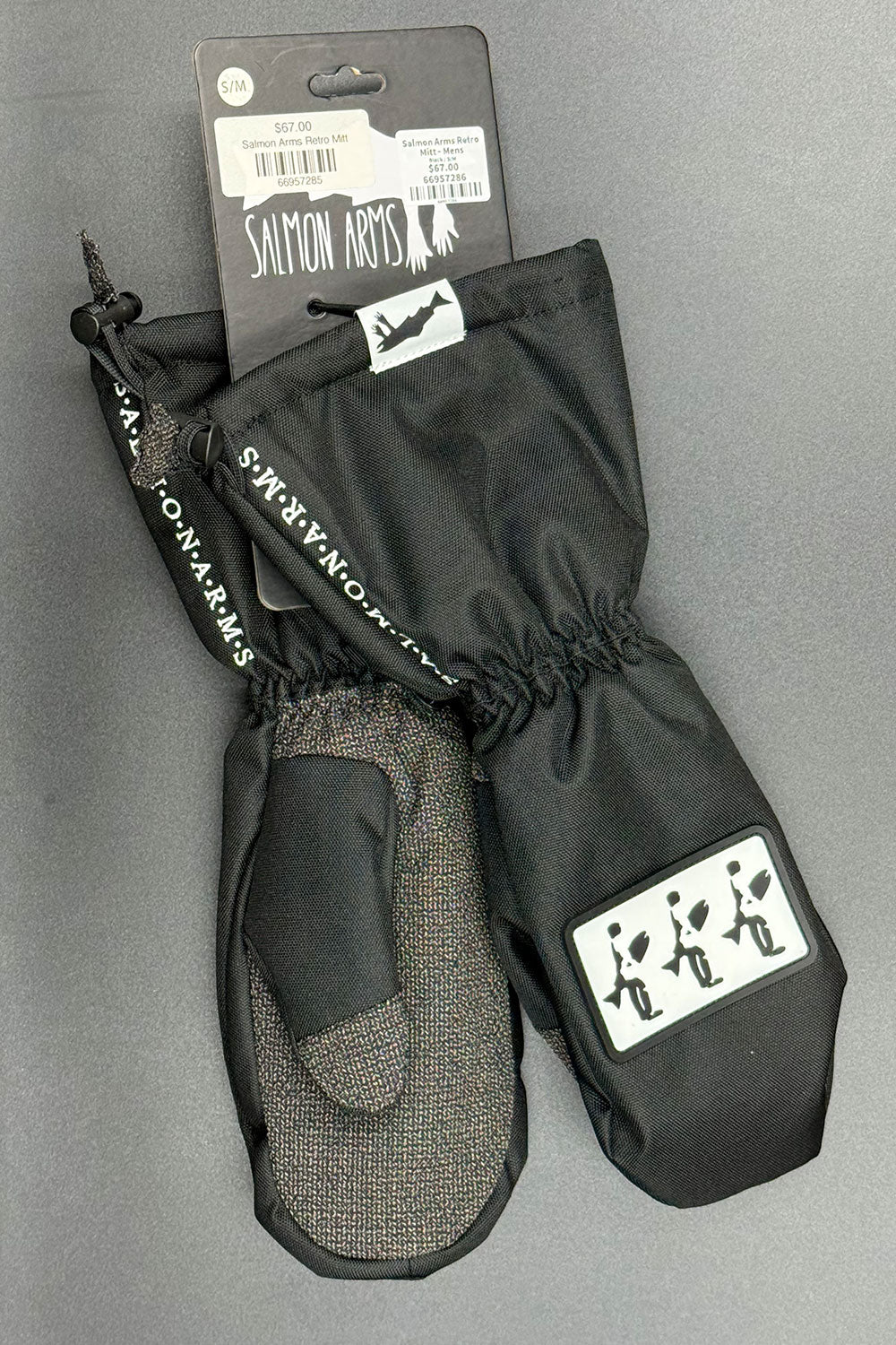 Pair of black mittens with gray interior on a gray background, featuring Salmon Arm's branding.