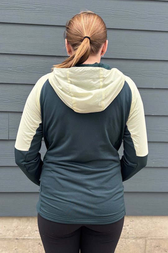 Person wearing a teal and beige hoodie standing against a gray wall.