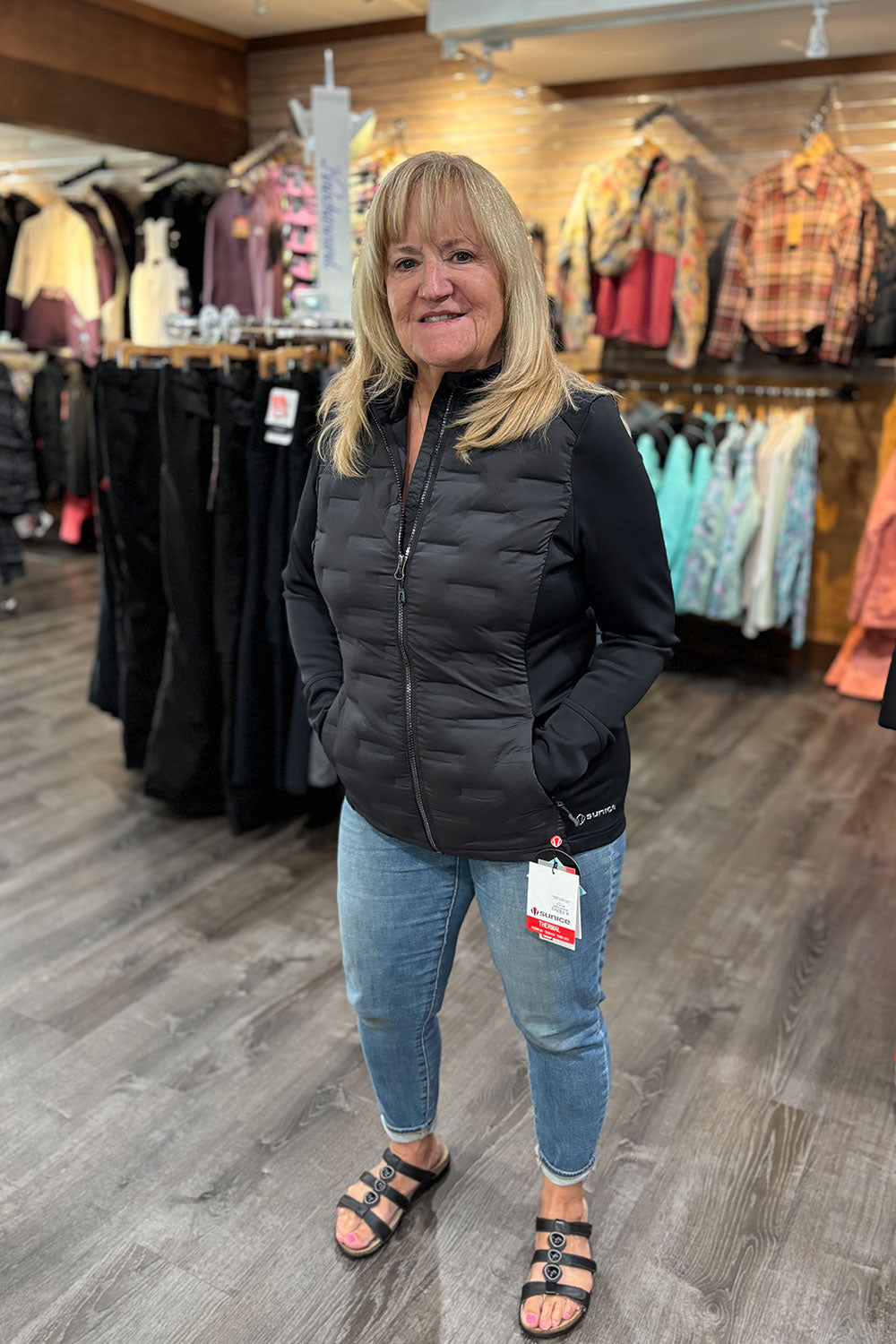 Woman wearing a black puffer jacket and jeans standing in a clothing store.