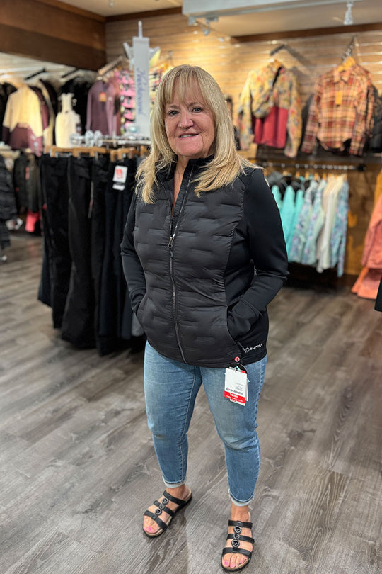 Woman wearing a black puffer jacket and jeans standing in a clothing store.