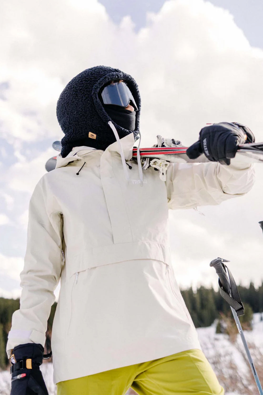 Person in winter gear with skis and poles against a snowy background