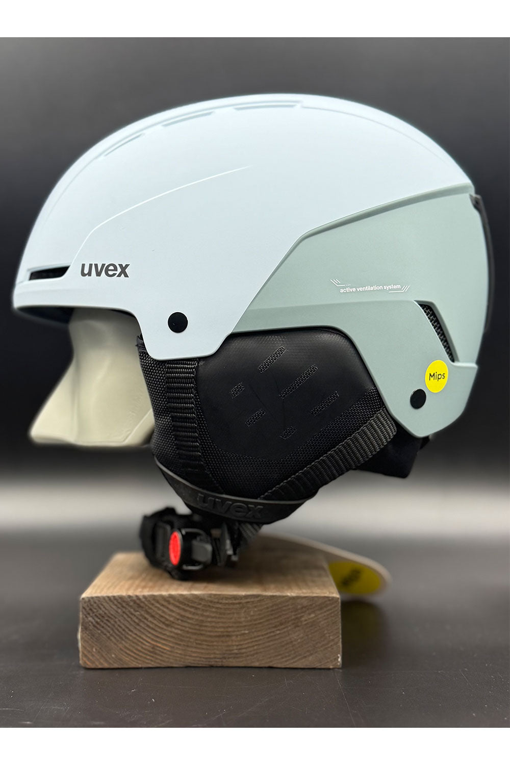 Light blue helmet with black chin strap on a wooden block against a dark background